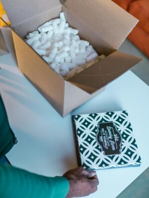 Open cardboard box with packing peanuts and hand placing patterned item.